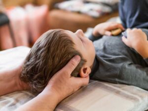 Person gently stretching a knee indoors beside a rainy window.